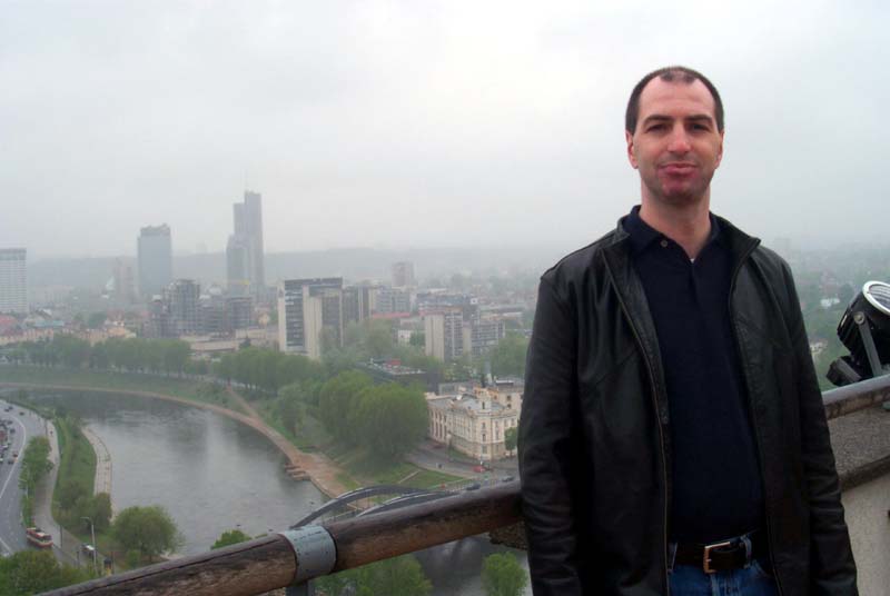 S on the observation deck at the top of the Vilnius castle, with some of the Vilnius newer neighborhoods and the Neris river visible behind him (May 2004)