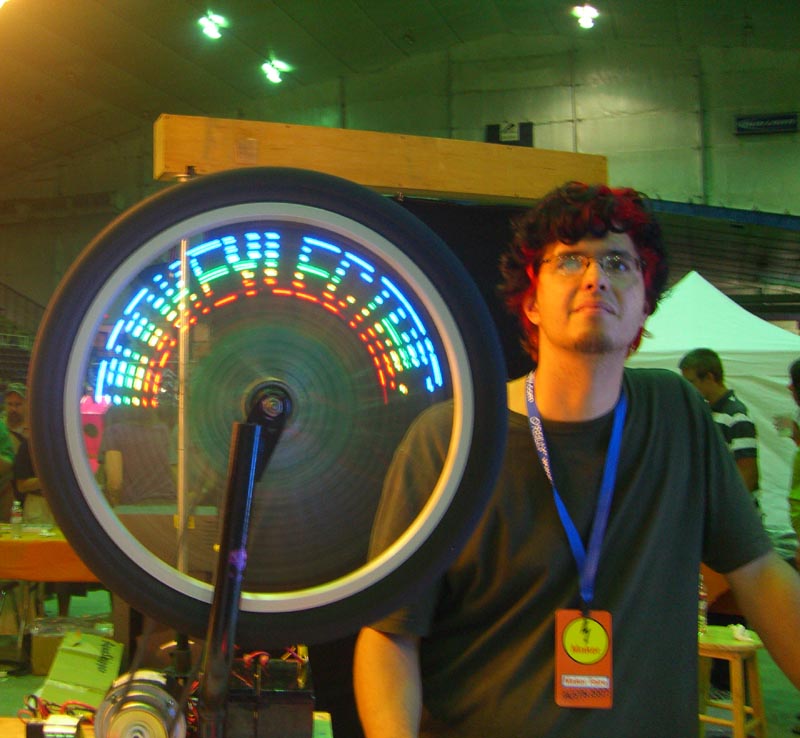 A spinning bicycle wheel with letters KEYLECTRIC, prefixed by 3-4 other, illegible, letters, seen at the Maker Faire 2007